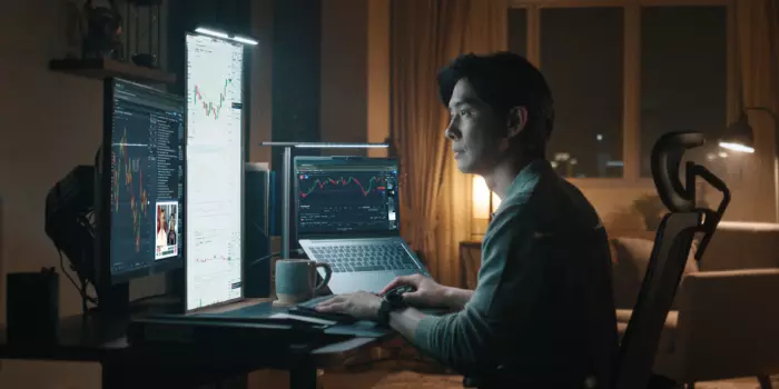 Trader using IG's multi-monitor setup to analyse charts and execute trades from home office