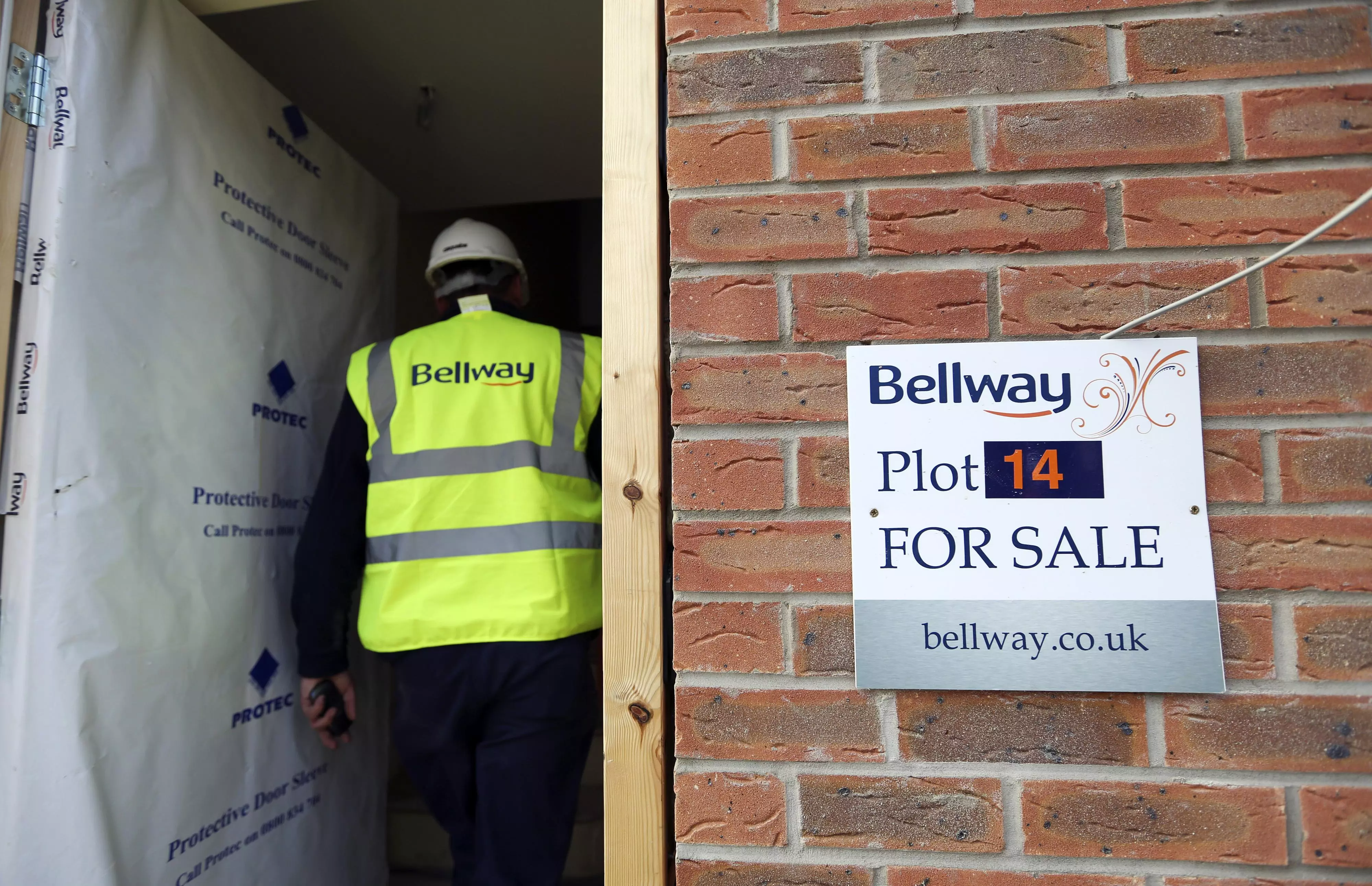Image of a Bellway "For Sale" sign on a brick wall, with a Bellway construction worker wearing a safety helment and visor walking into the building.